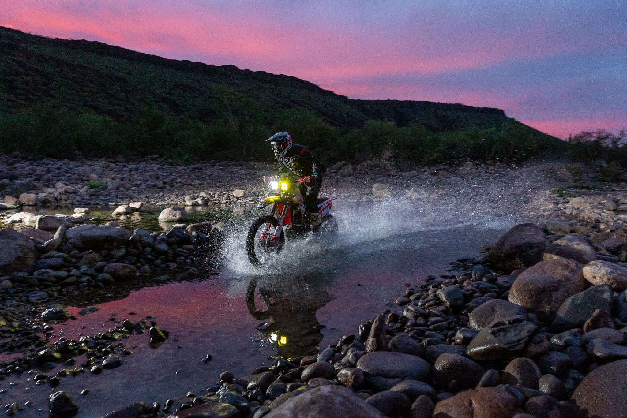 SCORE off-road motorcycle crossing rocky terrain and water during an earlier Baja race